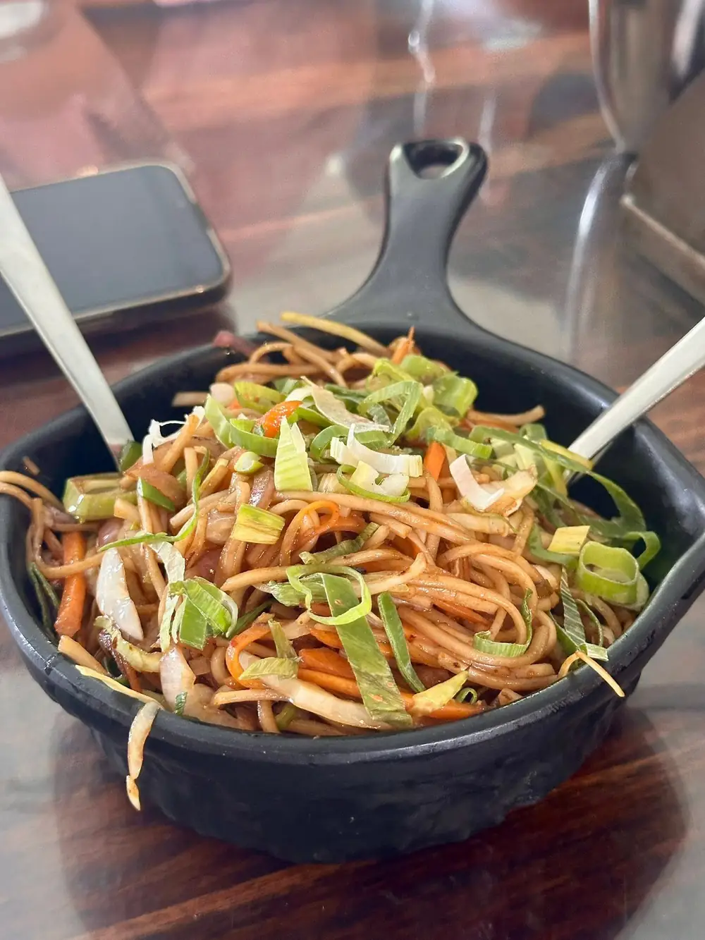 Desi chowmein in a black bowl topped with sliced spring onion