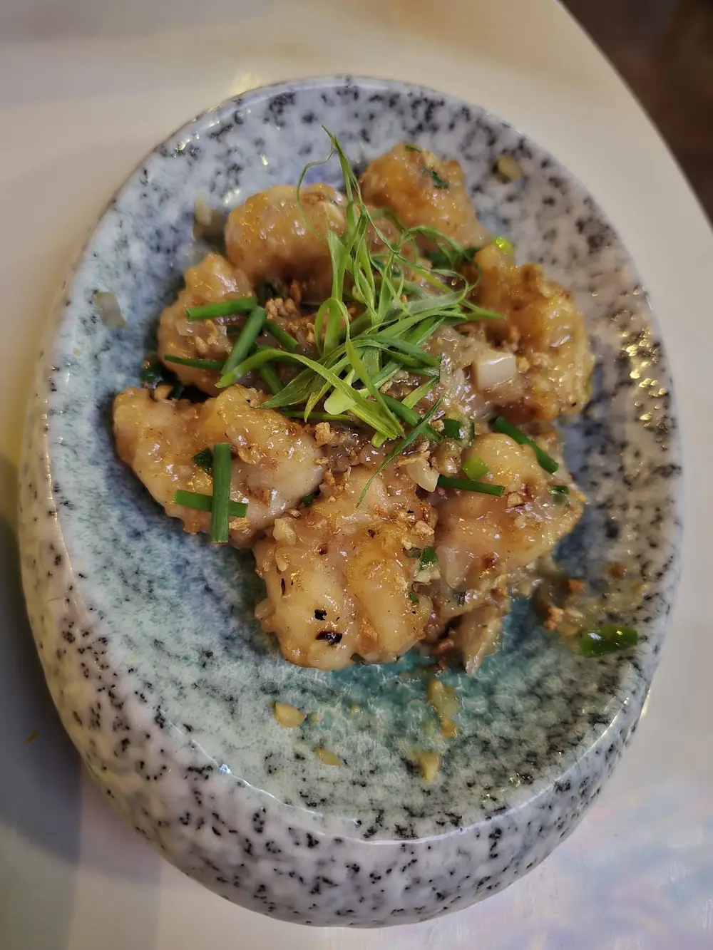 Garlic butter prawns topped with shredded spring onion on a speckled ceramic plate