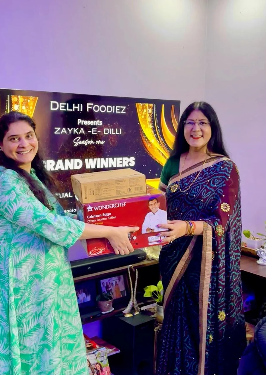 Anjali Saxena receiving her Wonderchef oven toaster griller from Jyoti Kohli in front of the Zayka-e-Dilli grand winners screen