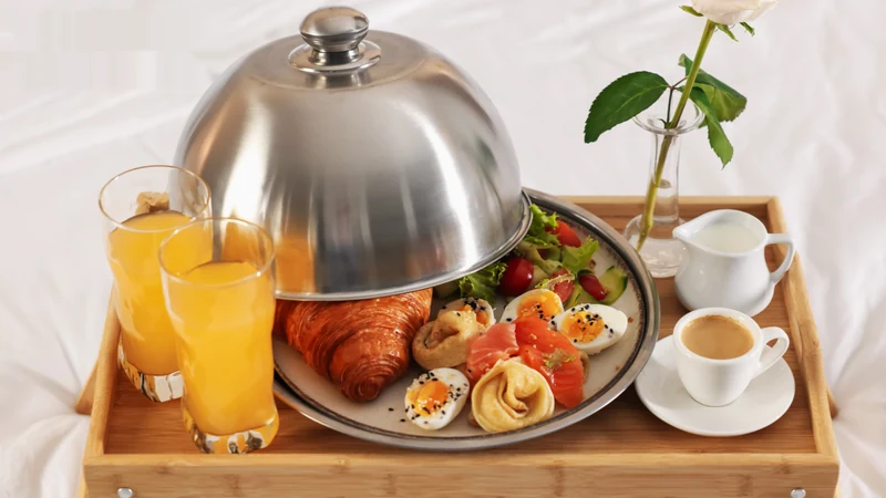 Hotel breakfast tray with a silver cloche, croissant, smoked salmon plate, orange juice and espresso