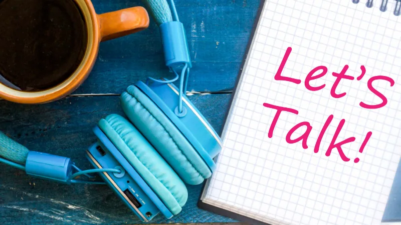 Headphones, a mug of black coffee and a notepad reading Lets Talk on a blue wooden table